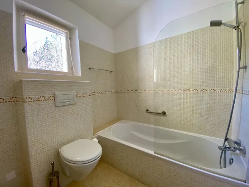 De badkamer met ligbad, douchescherm en hangend toilet