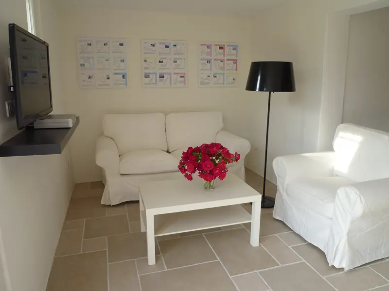 De zithoek met witte bank en fauteuil, rozen op tafel en de drie panelen met fietsroutes aan de muur